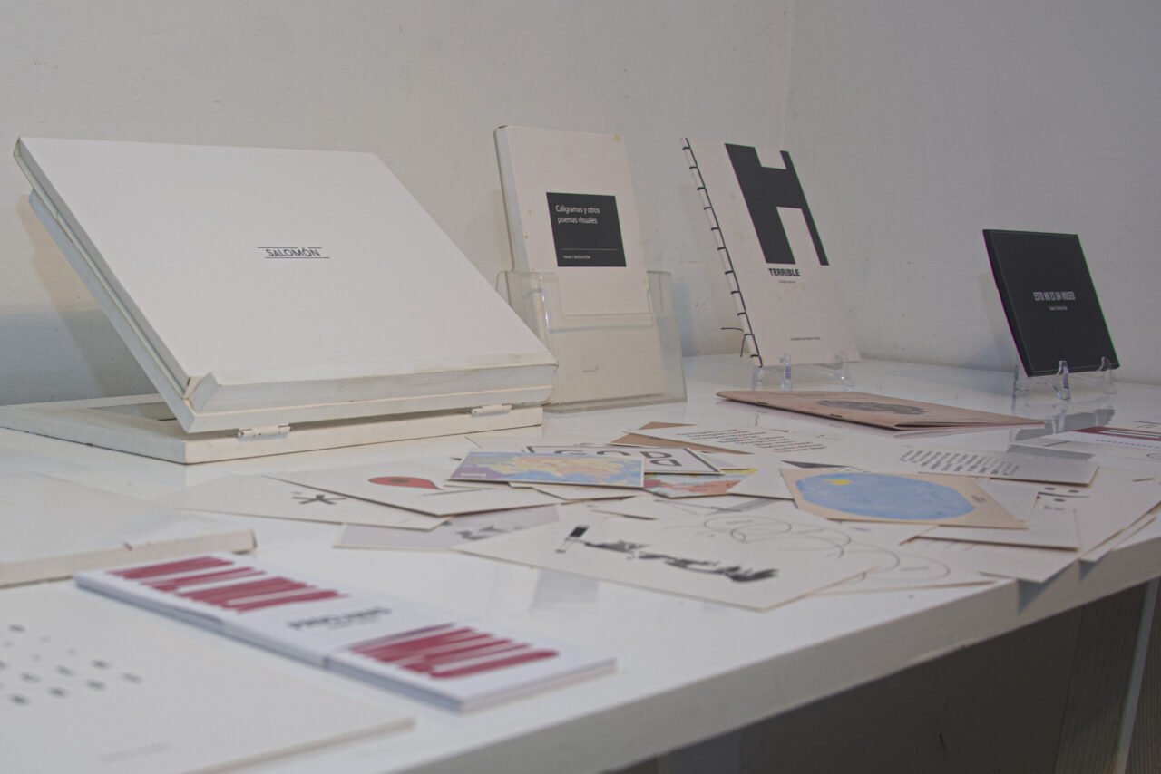Mesa expositiva blanca con publicaciones, cajas y postales de Ediciones Asterisco.