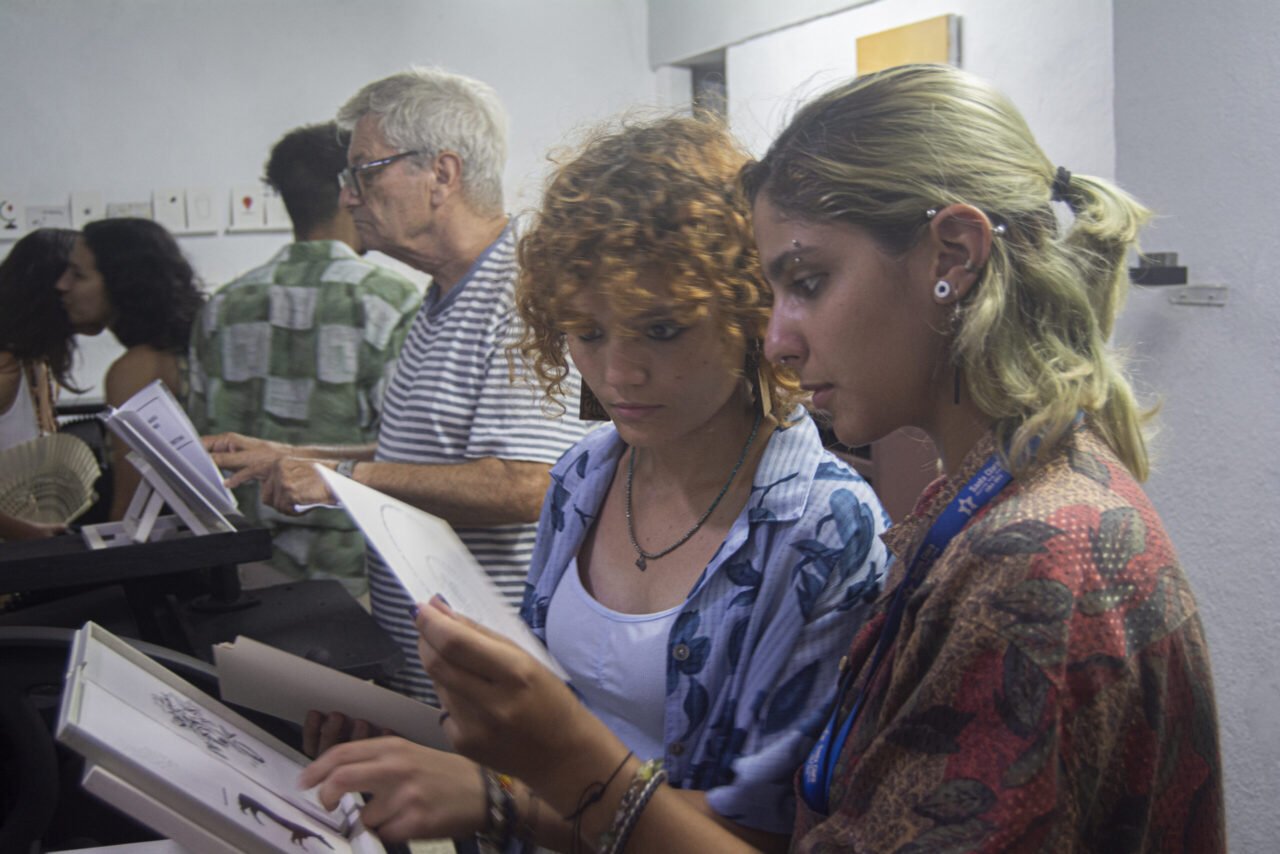 Tres personas de pie hojean publicaciones de Ediciones Asterisco durante una presentación.