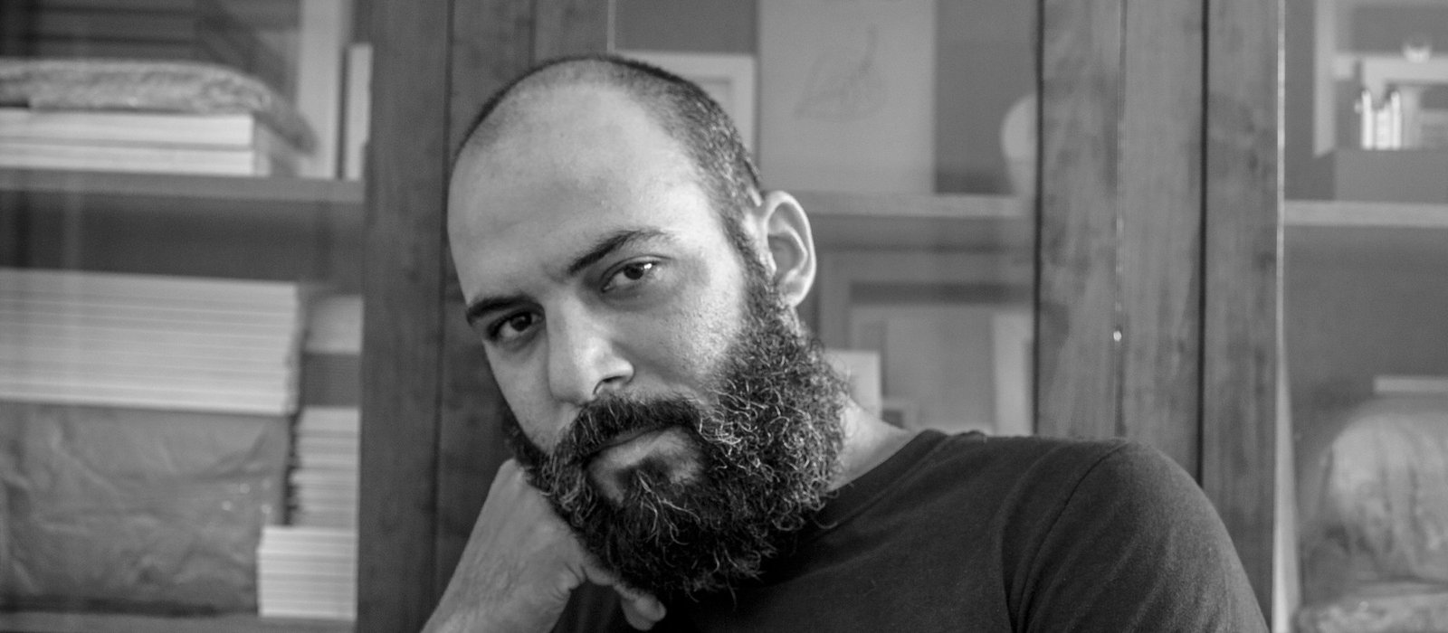 Yornel J. Martínez Elías apoyado en la mano, frente a una vitrina con libros y obra en su estudio